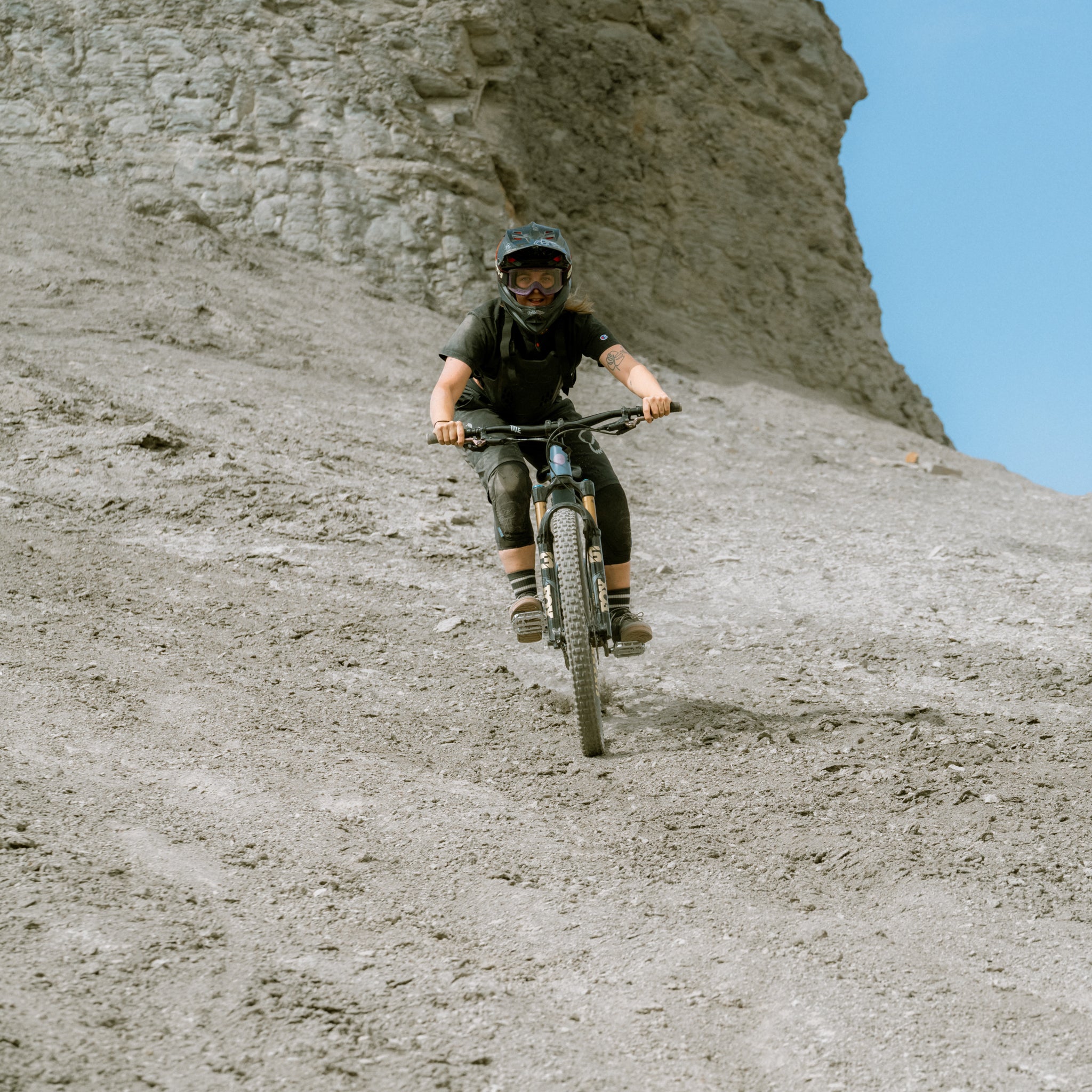 Person riding a bike on a rocky hillside with a clear sky.
